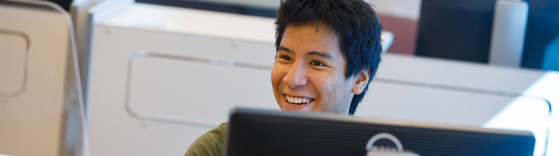 Male student in computer lab smiling and talking with counselor or adviser