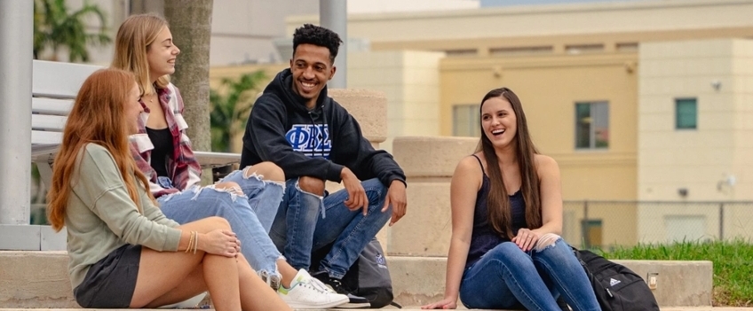 a group of diverse students conversing while sitting on steps on campus