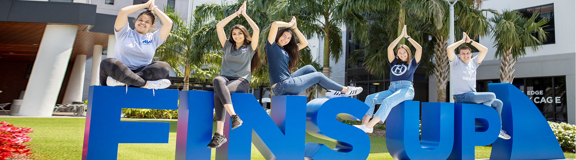 NSU students posing on NSU letters with fins up hands