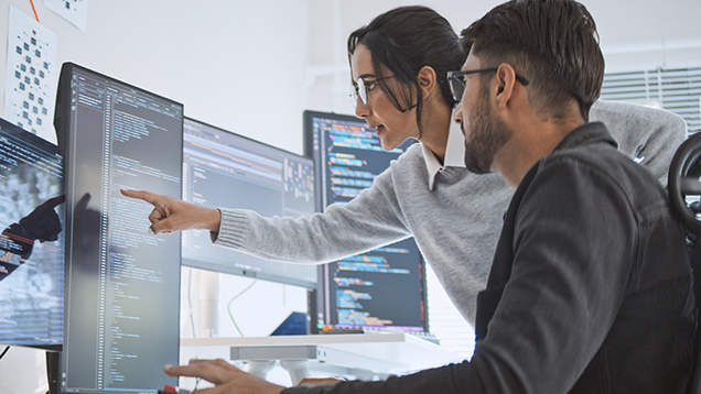 Two people looking at programming code on a computer screen