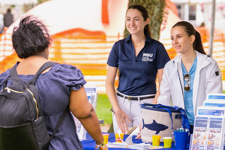 NSU students speaking to a woman at an outdoor event