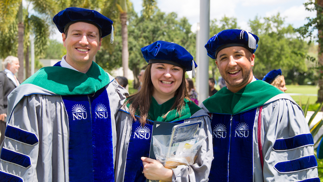Three students at graduation wearing regalia.