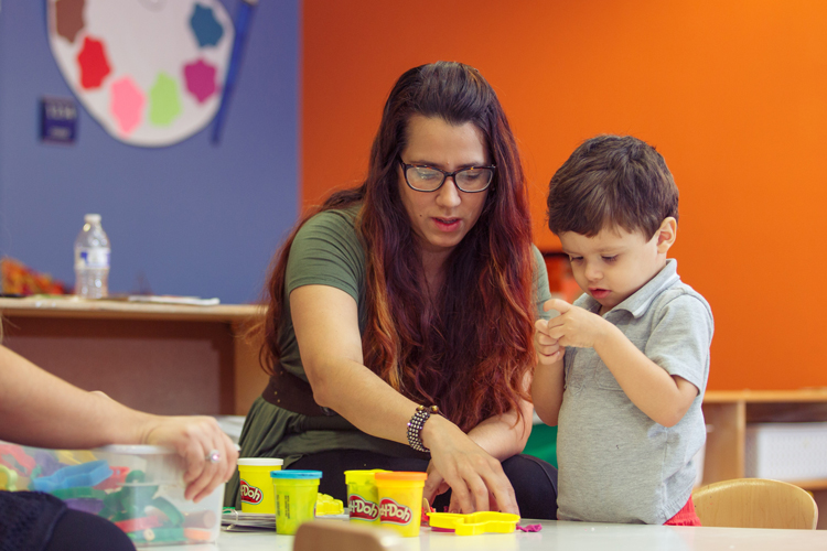 Early education teacher and child using play doh