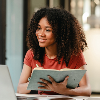 Student looking at her laptop and writing in a notebook