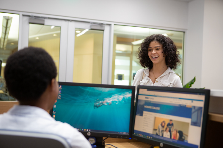 Two students talking over computer monitors