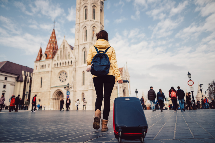 Student wearing a backpack and pulling roller suitcase in front of a church