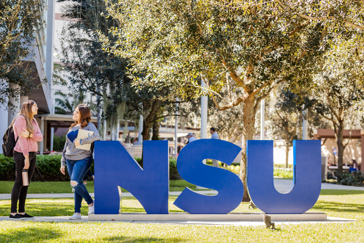 Two students talking next to large NSU letters