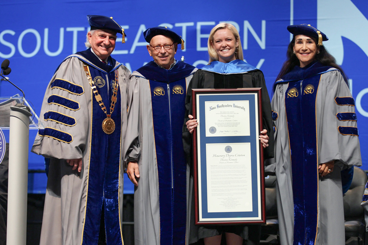 Honorary degree recipient holds framed certificate with the president and two robed faculty members
