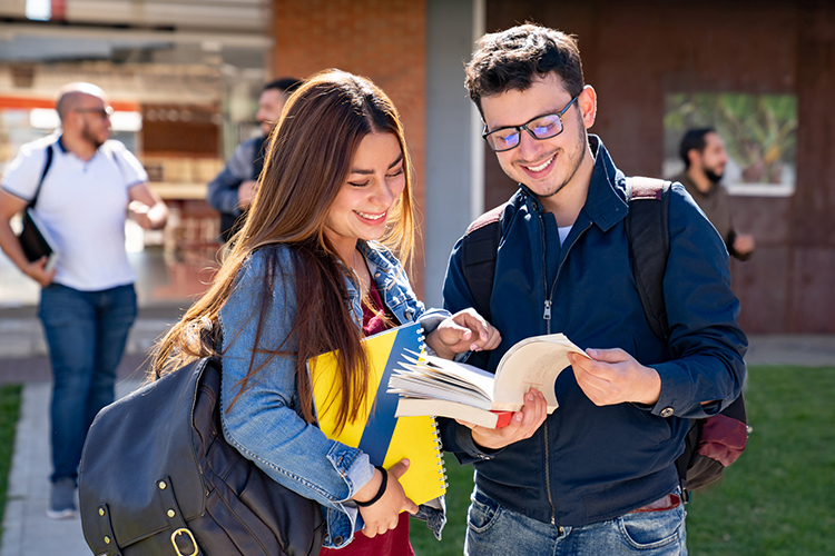Students looking at a book and smiling outdoors