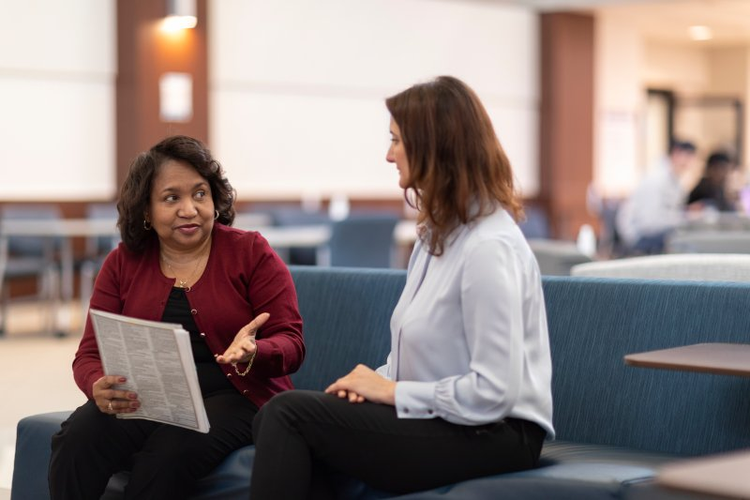 Women discussing documents on campus sofa