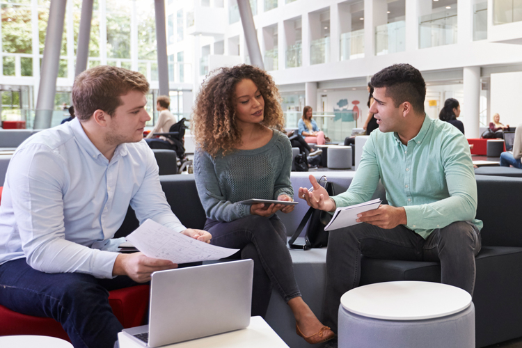 Three students sitting and talking in an atrium.