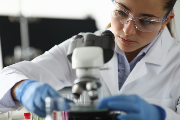 Female chemist investigating sample under microscope