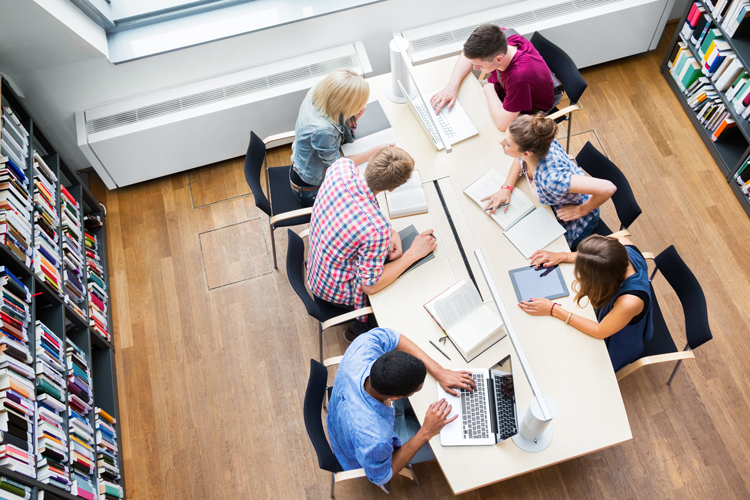 Overhead view of six students sitting in library with study materials.