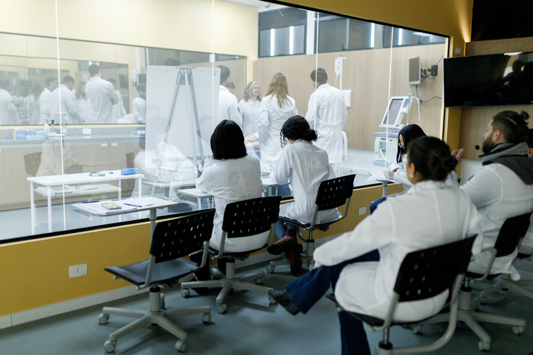 Medical students at clinical observing through glass window simulation lab