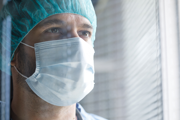 Medicine student with mask closeup looking through the window thinking