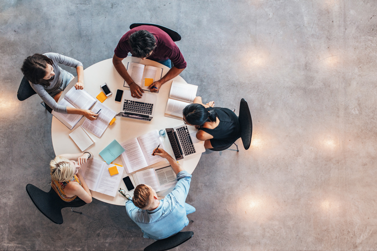 Overhead view of five students studying on table.