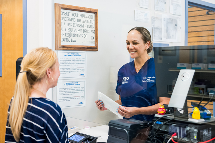 NSU health pharmacy technician attending patient thru the window