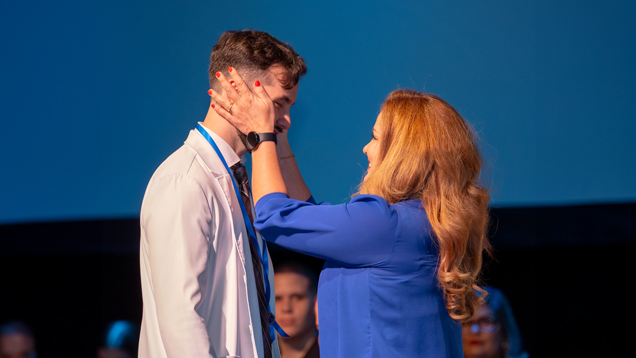 Male student on stage at Nursing Pinning Ceremony with family member