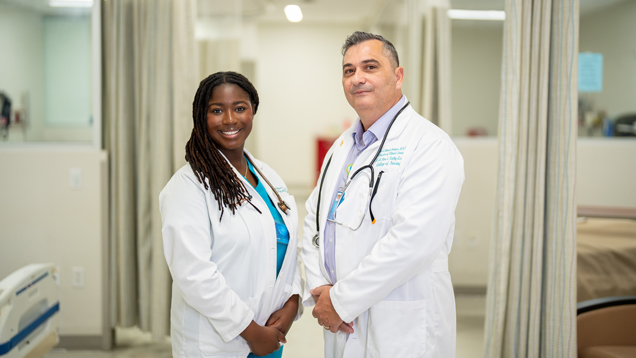 Professor and student wearing lab coats in hospital setting.