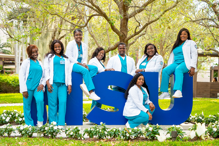 Group of nursing students posing for camera on NSU logo sculpture sign