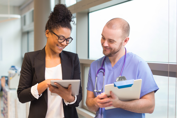 Lady with professional attire speaking and showing digital tablet to nurse