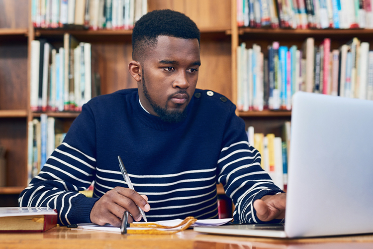 Student taking notes while using a laptop