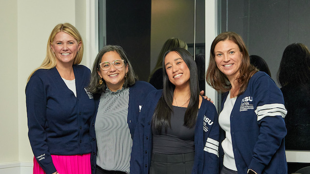 Four graduate students wearing cardigans with arms around each other.