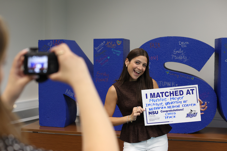 Happy student holding match day sign and large NSU letters in background.