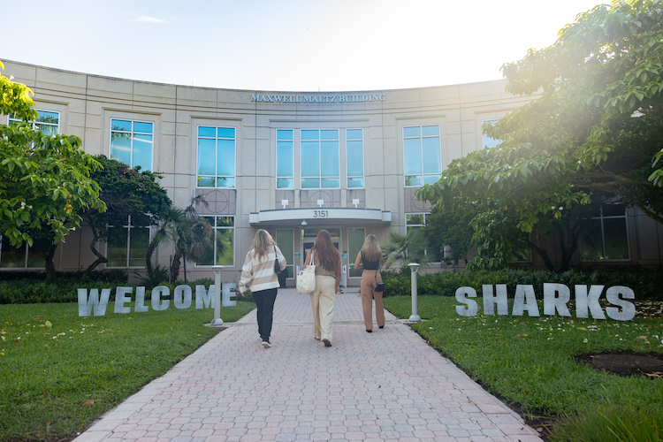 Students walking into Maltz Buiding with the words "Welcome Students" in the lawn.