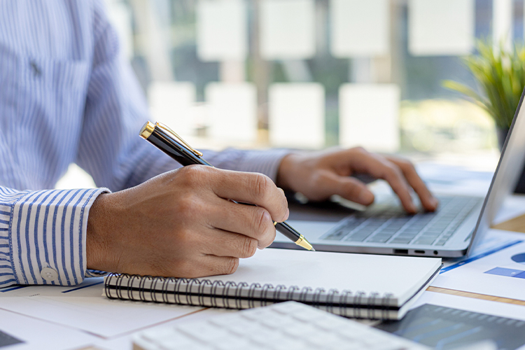 Man using a laptop and taking notes in an office close up