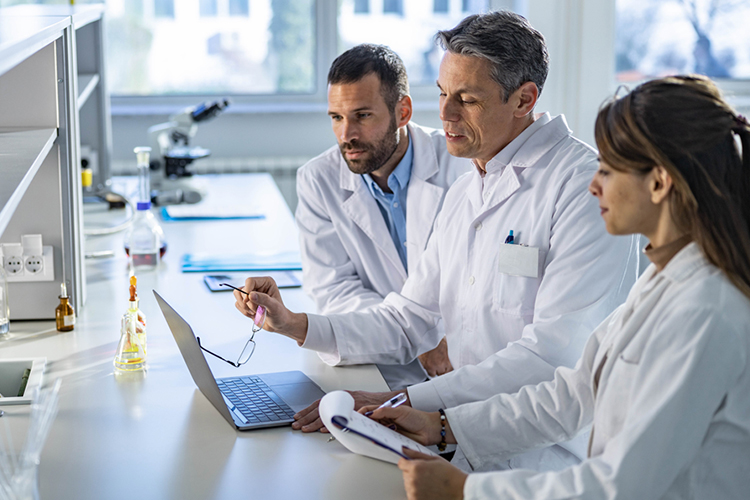 Team of scientists using a laptop and taking notes in a lab