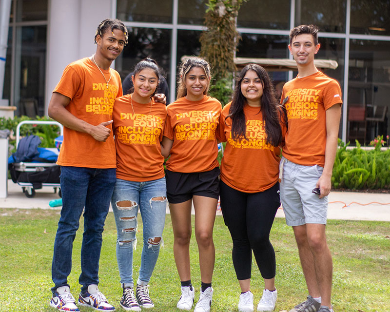 five smiling students wearing orange DEIB shirts