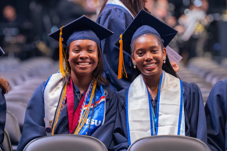 two-graduates-smiling-seated-in-ceremony